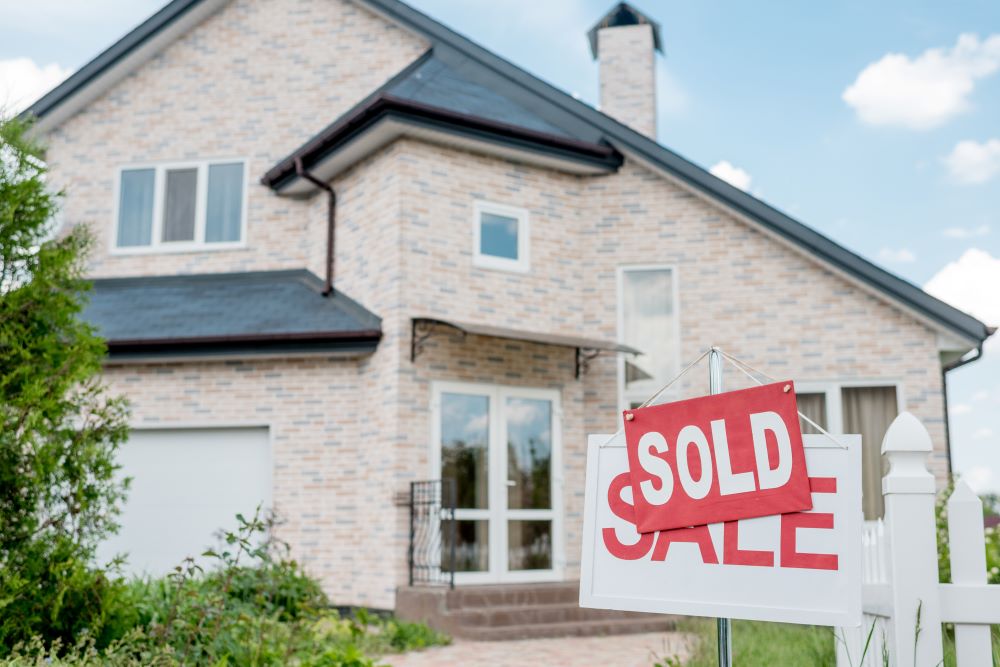 Close up view of sold sign on wooden placard with sale sign in front of modern cottage